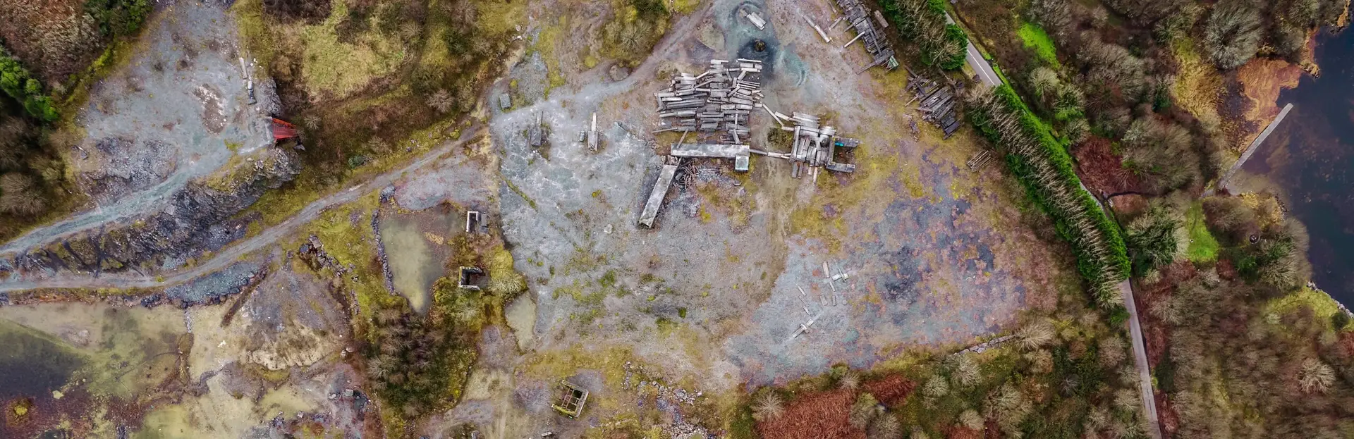 Aerial view of a brownfield site with scattered debris, ponds, and surrounding vegetation, illustrating potential reptile habitats. ACP Provide Reptile Survey for Planning and Development.